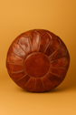 Brown leather pouf on a matching orange background